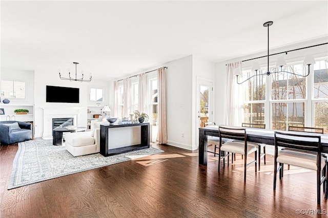 dining area with baseboards, a glass covered fireplace, wood finished floors, and a notable chandelier