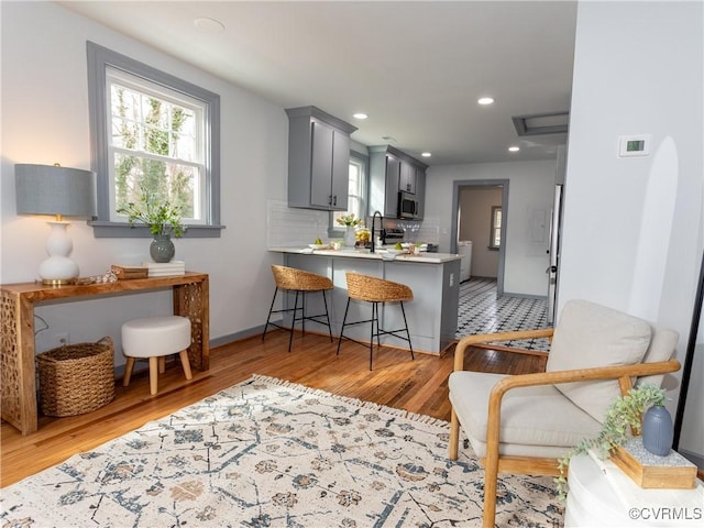 kitchen with tasteful backsplash, light countertops, stainless steel microwave, light wood-style flooring, and a peninsula