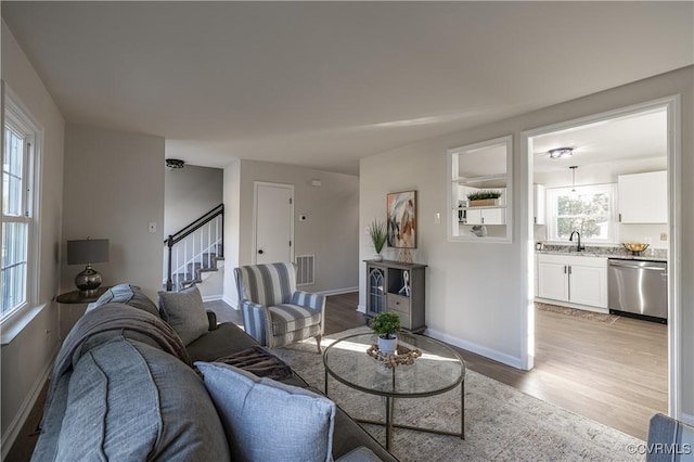 living room with baseboards, stairway, visible vents, and light wood-style floors