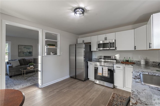 kitchen featuring light stone counters, stainless steel appliances, white cabinets, a sink, and wood finished floors