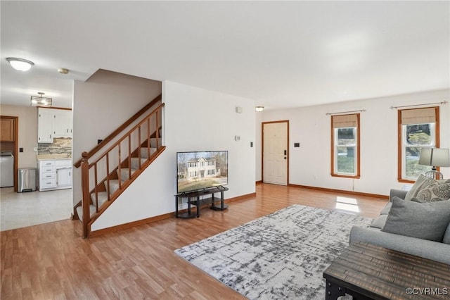 living room featuring light wood-style flooring, washer / dryer, stairway, and baseboards