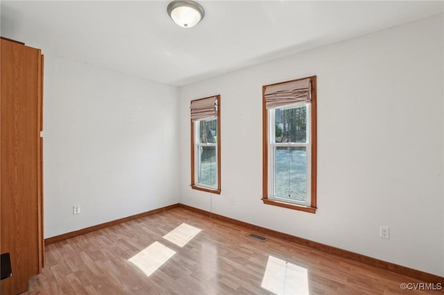 spare room featuring light wood-type flooring, visible vents, and baseboards