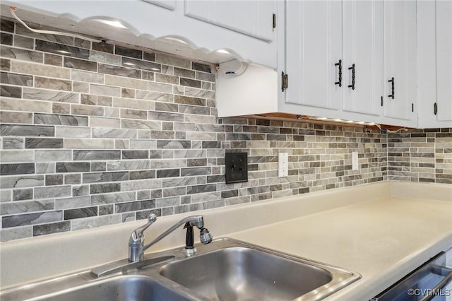 kitchen featuring tasteful backsplash, light countertops, white cabinets, and a sink