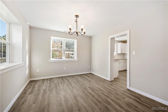 unfurnished dining area with baseboards, a chandelier, and wood finished floors