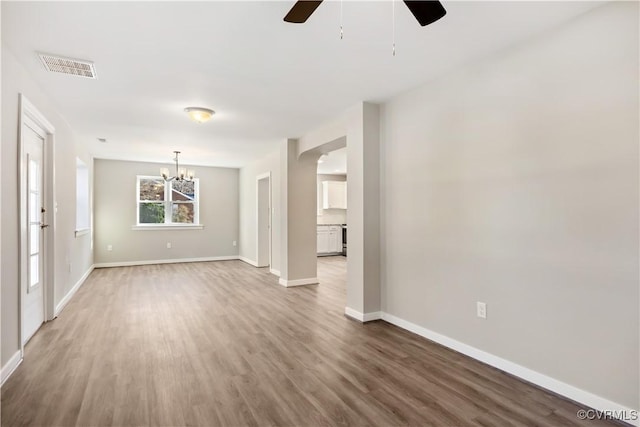 empty room with arched walkways, ceiling fan with notable chandelier, wood finished floors, visible vents, and baseboards