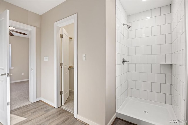 bathroom with ceiling fan, baseboards, a tile shower, and wood finished floors