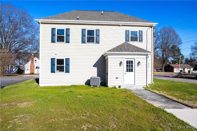 rear view of property with roof with shingles, cooling unit, and a yard