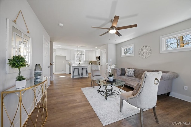 living room with ceiling fan with notable chandelier, wood finished floors, and baseboards