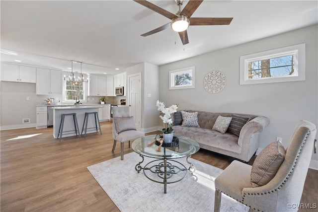 living room with ceiling fan with notable chandelier, light wood finished floors, visible vents, and baseboards