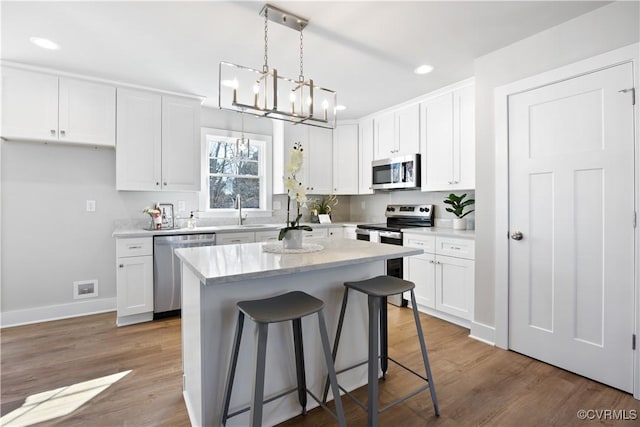 kitchen featuring a notable chandelier, stainless steel appliances, wood finished floors, a kitchen island, and white cabinets