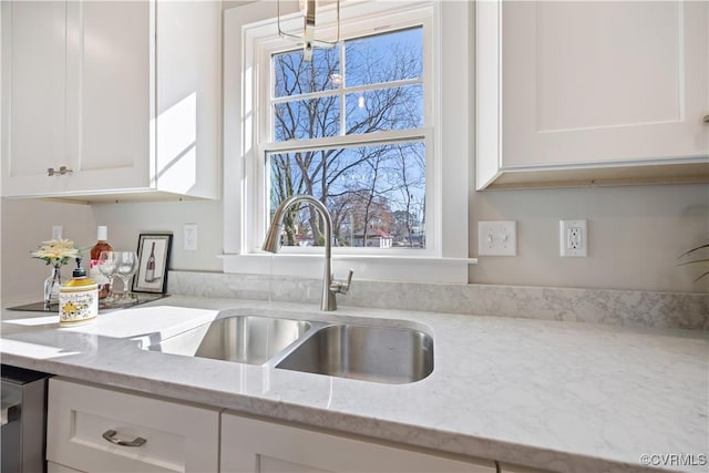 kitchen featuring light stone counters, white cabinets, and a sink