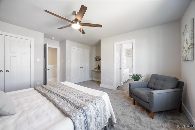 bedroom with baseboards, ensuite bath, a ceiling fan, and two closets