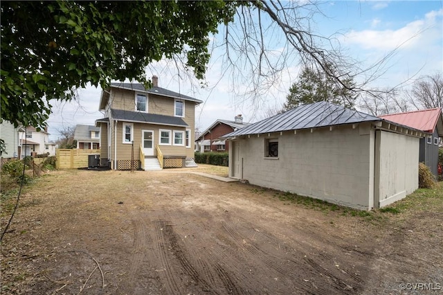 rear view of house with fence, entry steps, a chimney, metal roof, and concrete block siding