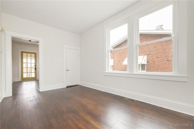 empty room with dark wood-style floors, visible vents, and baseboards