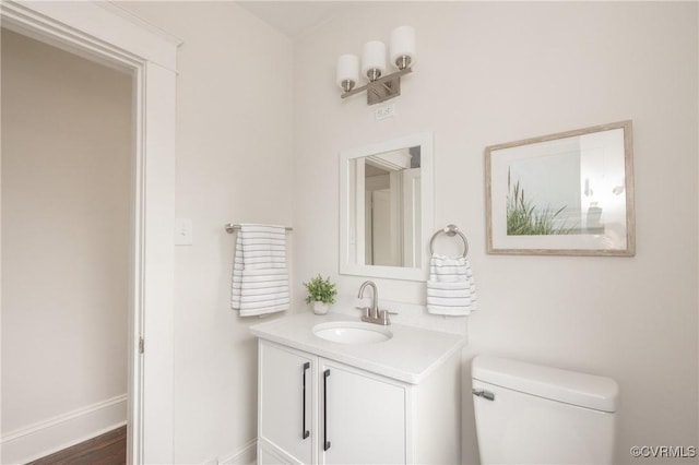 half bathroom featuring baseboards, toilet, and vanity