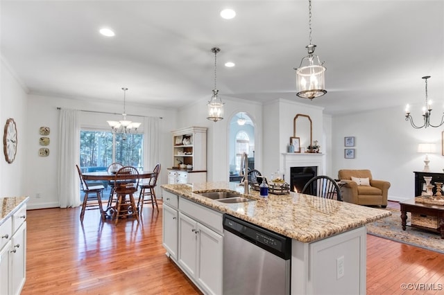 kitchen with stainless steel dishwasher, an inviting chandelier, light wood-style floors, a sink, and a warm lit fireplace