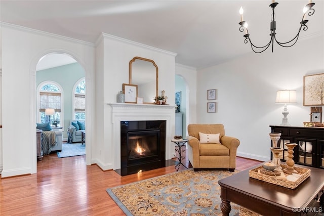 living area with a fireplace with flush hearth, crown molding, baseboards, and wood finished floors