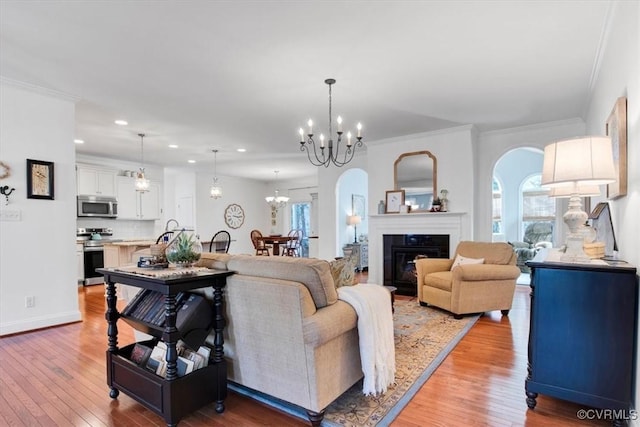 living area featuring a notable chandelier, light wood finished floors, a wealth of natural light, ornamental molding, and a glass covered fireplace