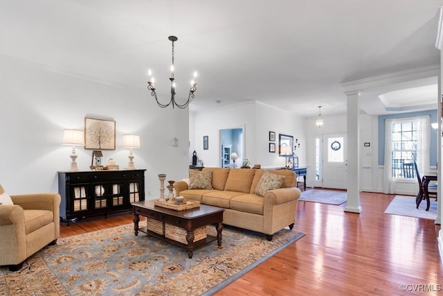 living area with a notable chandelier, ornate columns, and wood finished floors