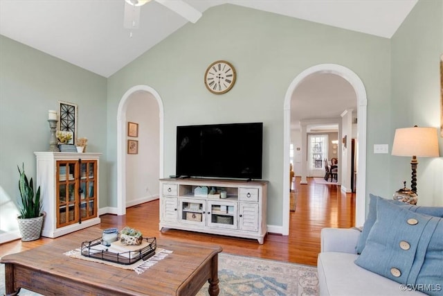 living room with arched walkways, high vaulted ceiling, wood finished floors, a ceiling fan, and baseboards