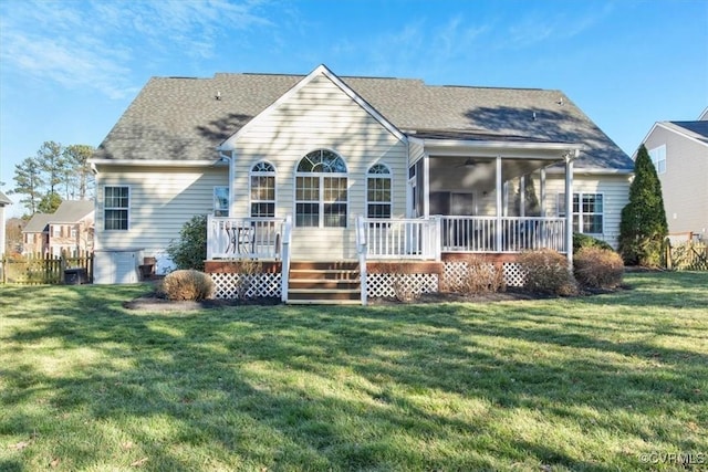 back of house featuring a deck, a yard, roof with shingles, and a sunroom