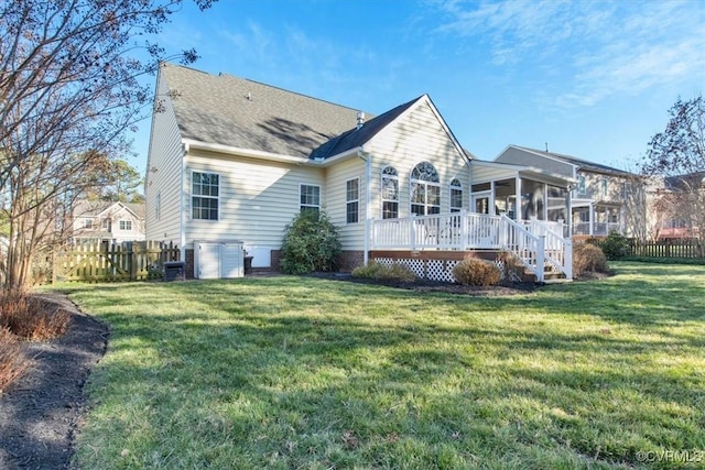 rear view of property featuring a sunroom, fence, a wooden deck, and a lawn