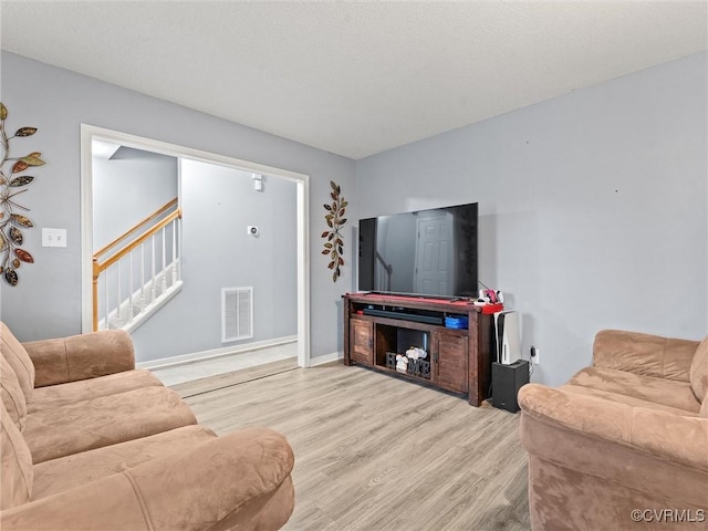 living area with stairs, wood finished floors, visible vents, and baseboards