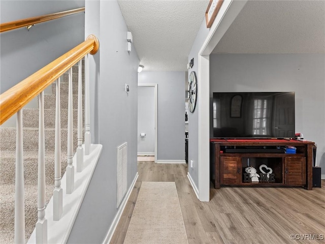 corridor featuring baseboards, visible vents, wood finished floors, stairs, and a textured ceiling