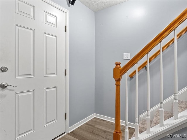 foyer featuring a textured ceiling, stairway, baseboards, and wood finished floors