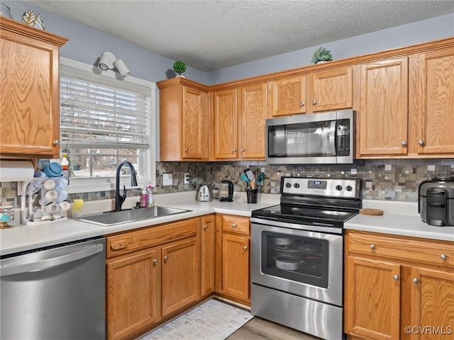 kitchen with a textured ceiling, a sink, light countertops, appliances with stainless steel finishes, and backsplash