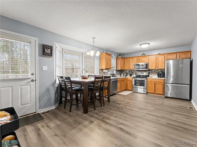 kitchen with plenty of natural light, appliances with stainless steel finishes, light wood-type flooring, and decorative backsplash