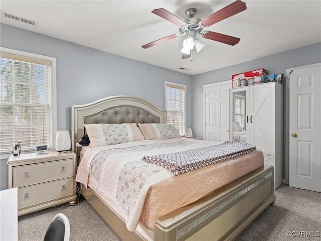 bedroom with a ceiling fan, visible vents, a textured ceiling, and light colored carpet