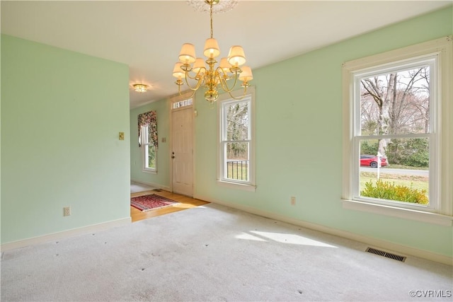 carpeted spare room with a notable chandelier, visible vents, and baseboards