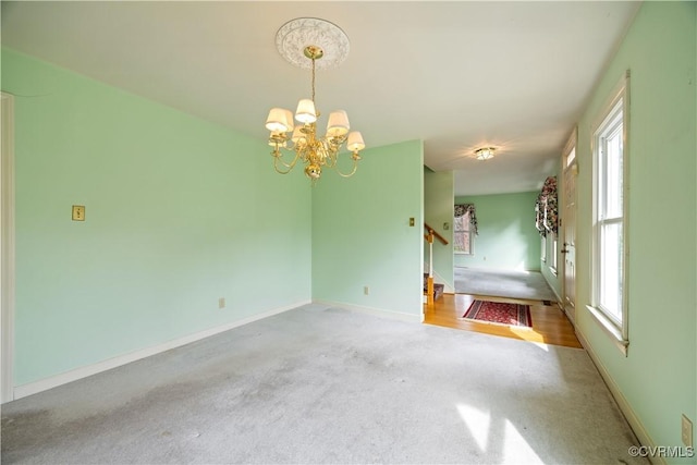 unfurnished room featuring a healthy amount of sunlight, baseboards, an inviting chandelier, and carpet floors