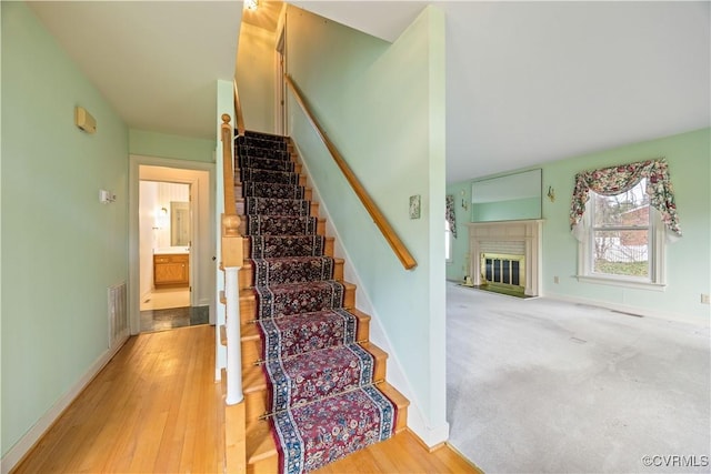 stairway featuring a glass covered fireplace, visible vents, and baseboards