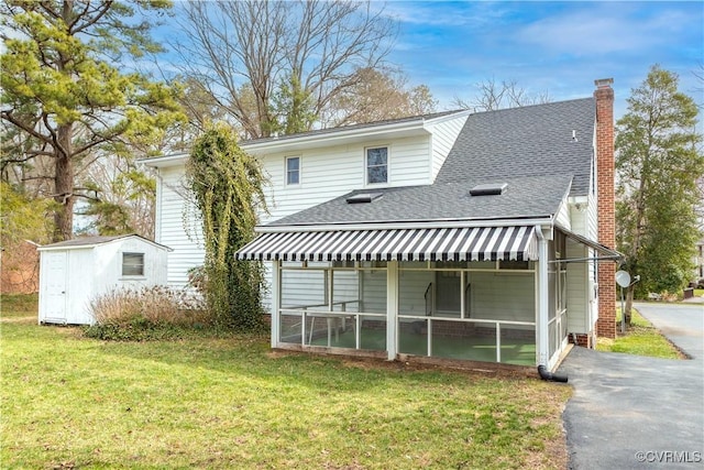 rear view of house featuring an outbuilding, a yard, roof with shingles, a sunroom, and a chimney