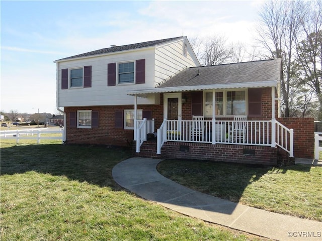 split level home with brick siding, roof with shingles, a porch, and a front yard