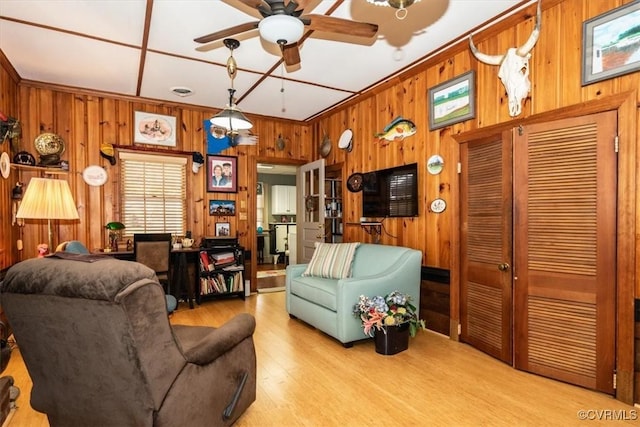 living room with a ceiling fan, visible vents, wood walls, and wood finished floors