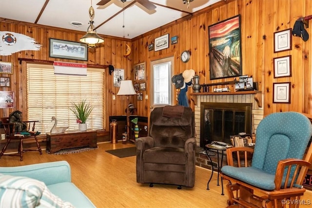 living room featuring wooden walls, visible vents, a ceiling fan, wood finished floors, and a fireplace