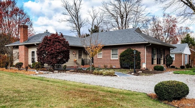 single story home featuring gravel driveway, a chimney, a front lawn, and brick siding