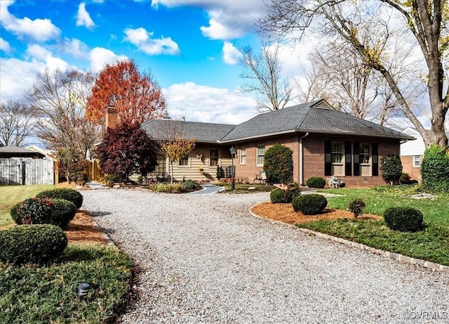 view of front of property with brick siding, a chimney, gravel driveway, and fence