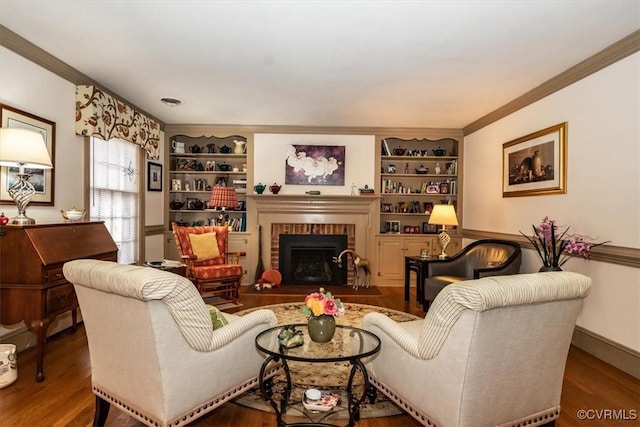 living room featuring ornamental molding, a brick fireplace, wood finished floors, and built in shelves