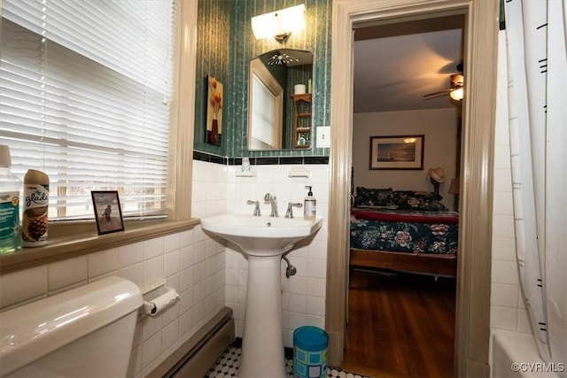 bathroom with a bathtub, tile walls, baseboard heating, toilet, and a sink