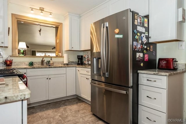 kitchen with light stone counters, stove, white cabinetry, stainless steel refrigerator with ice dispenser, and a sink