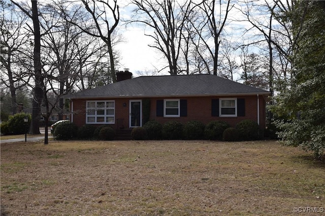 view of front facade featuring brick siding, a chimney, and a front yard