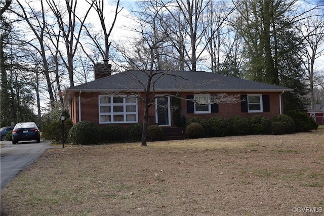 single story home featuring driveway, brick siding, a front lawn, and a chimney