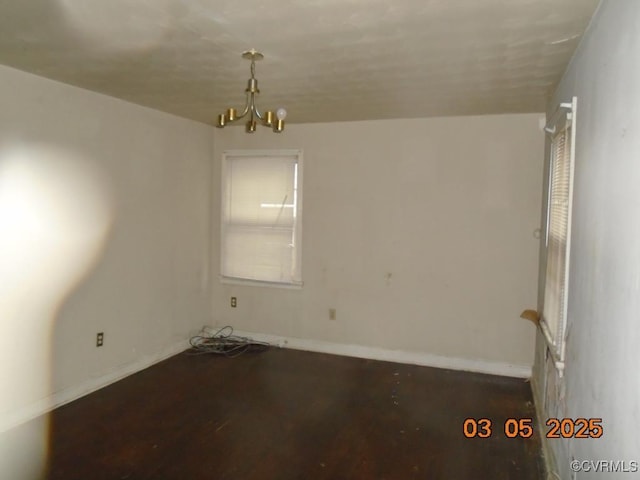 spare room featuring wood finished floors, baseboards, and an inviting chandelier