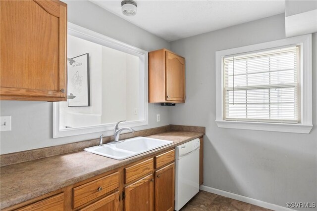 kitchen featuring white dishwasher, baseboards, and a sink