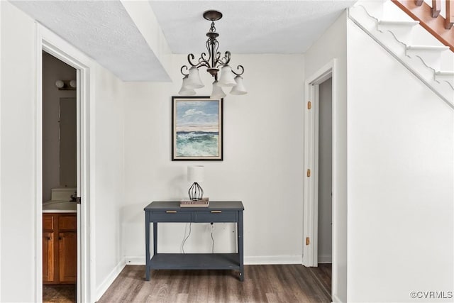 corridor featuring a notable chandelier, a textured ceiling, wood finished floors, and baseboards