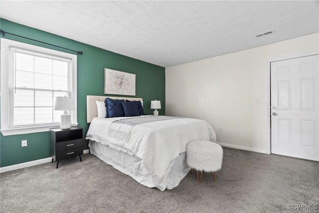 bedroom with carpet floors, visible vents, a textured ceiling, and baseboards